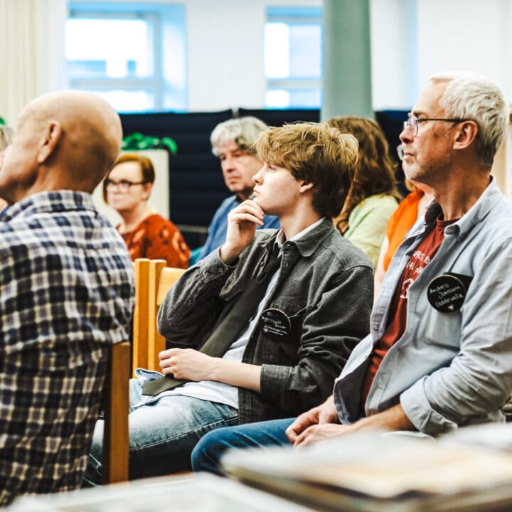 Bilden visar en grupp människor som sitter på stolar och verkar vara fokuserade på något som pågår ...